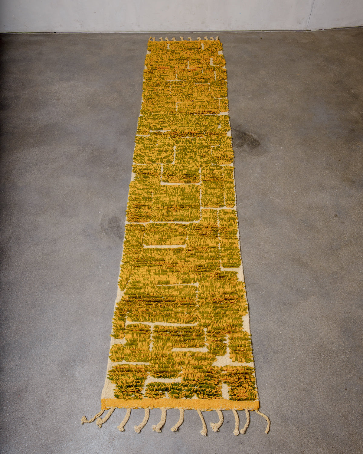 Berberlin Berber runner rug in mixed yellow and olive green wool, laying flat on concrete floor.